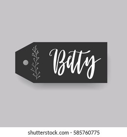 Girl name Betty. Calligraphy lettering. Black badge decorated with botanical element and female name. Can be used as place card on wedding or anniversary.