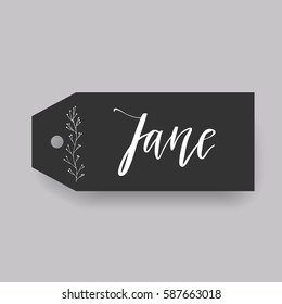 Girl name Jane. Calligraphy lettering. Black badge decorated with botanical element and female name. Can be used as place card on wedding or anniversary.