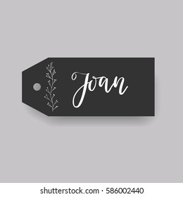 Girl name Joan. Calligraphy lettering. Black badge decorated with botanical element and female name. Can be used as place card on wedding or anniversary.