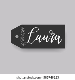 Girl name Laura. Calligraphy lettering. Black badge decorated with botanical element and female name. Can be used as place card on wedding or anniversary.