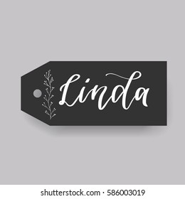 Girl name Linda. Calligraphy lettering. Black badge decorated with botanical element and female name. Can be used as place card on wedding or anniversary.