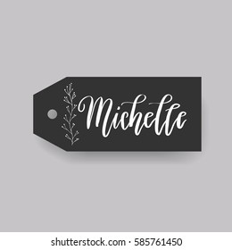 Girl name Michelle. Calligraphy lettering. Black badge decorated with botanical element and female name. Can be used as place card on wedding or anniversary.