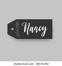 Girl name Nancy. Calligraphy lettering. Black badge decorated with botanical element and female name. Can be used as place card on wedding or anniversary.