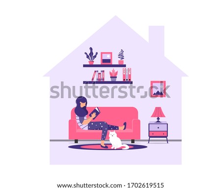 Girl is reading a book while sitting on a sofa. A young woman is relaxing at home on the couch with a book and a cat. Stay home during a pandemic. Coronavirus prevention concept. 
