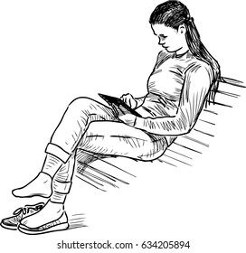 A girl reads a book on a park bench