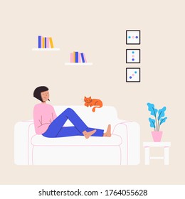 A girl relaxing at home sitting on the cozy couch with her cat, plants and books