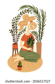 Сute girl sits on a rug surrounded by house plants and hugs a pot with a indoor flower.