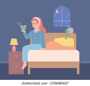 A girl is sitting in bed in the middle of the night holding an alarm clock. She is insomnia. flat design style minimal vector illustration.