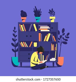 Girl sitting on the floor reads a book against the background of a bookcase. Home leisure.