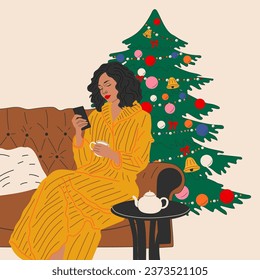 The girl is sitting on the sofa near the Christmas tree.  Hygge concept. Cozy winter days