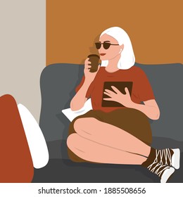 Girl sitting on the sofa at the window studying from home on her tablet and drinking coffee