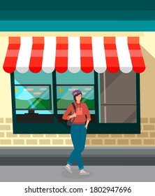 Girl in sportswear in a hat carries a backpack on her shoulder. Stylish young female chracter standing in the background of an electronics storefront. Woman with short dark hair in jeans and a sweater