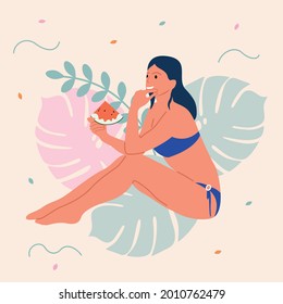 Girl in a swimsuit eating a watermelon on the beach against the backdrop of scenery