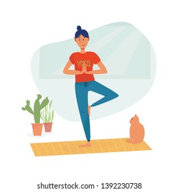Girl in t shirt with sign Yoga in tree pose practice asana balance exercise at home with smile, cat sitting behind. Healthy, home training with pet and sport activity concept. 