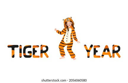 Girl in tiger carnival costume and inscription New Year from striped orange with black letters. Children pajama party or holiday. Kid in jumpsuits or kigurumi, festive clothing for Christmas
