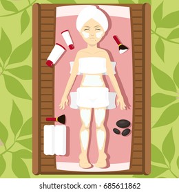 A girl in a towel lies in a spa center with a mask on her body surrounded by cosmetology