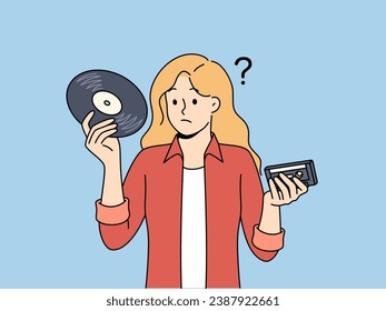 Girl with vinyl record and tape cassette looks confusedly at old-fashioned storage media with music. Woman feels confused and doesn know how to listen to music stored on vintage storage devices.