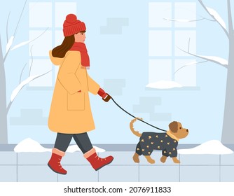 A girl in a warm coat, gloves, a hat and a scarf around her neck is walking with a dog down the winter street. A small dog in a grey jumpsuit. Vector illustration in flat style