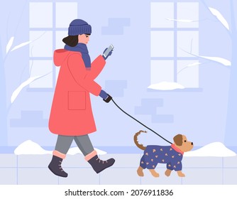 A girl in a warm coat, hat and gloves walks with a dog down the winter street and looks at the phone. A small dog in a blue jumpsuit. Vector illustration in flat style