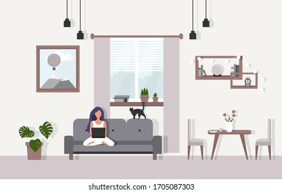 Girl working at home with cat sitting on sofa with laptop. Cute interior design with flowers, books and wall picture.