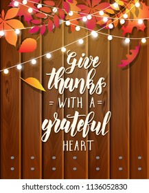 Give thanks with a grateful heart -  Thanksgiving day lettering calligraphy phrase on festive wooden background with autumn leaves and garland