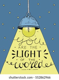 Glowing light bulb on long cord, casting beam of light. Lettering by hand You are the light of the world. Biblical background. Christian poster.