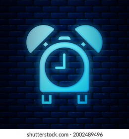 Glowing neon Alarm clock icon isolated on brick wall background. Wake up, get up concept. Time sign.  Vector