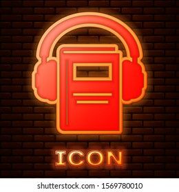 Glowing neon Audio book icon isolated on brick wall background. Book with headphones. Audio guide sign. Online learning concept.  Vector Illustration