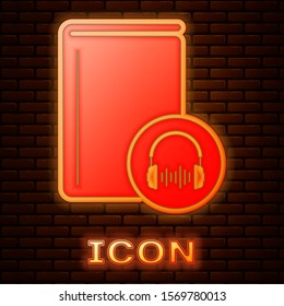 Glowing neon Audio book icon isolated on brick wall background. Book with headphones. Audio guide sign. Online learning concept.  Vector Illustration