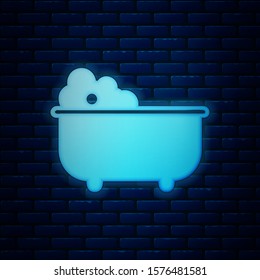 Glowing neon Baby bathtub with foam bubbles inside icon isolated on brick wall background.  Vector Illustration