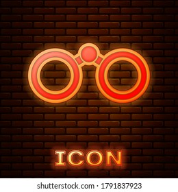 Glowing neon Binoculars icon isolated on brick wall background. Find software sign. Spy equipment symbol.  Vector Illustration