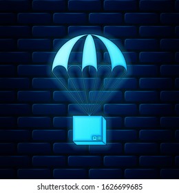 Glowing neon Box flying on parachute icon isolated on brick wall background. Parcel with parachute for shipping. Delivery service, air shipping concept, bonus concept.  Vector Illustration
