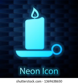 Glowing neon Burning candle in candlestick icon isolated on brick wall background. Old fashioned lit candle. Cylindrical aromatic candle stick with burning flame. Vector Illustration