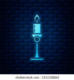 Glowing neon Burning candle in candlestick icon isolated on brick wall background. Old fashioned lit candle. Cylindrical candle stick with burning flame.  Vector Illustration
