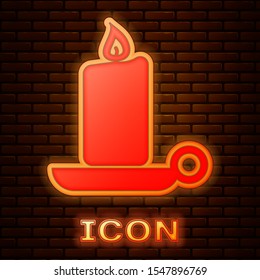 Glowing neon Burning candle in candlestick icon isolated on brick wall background. Old fashioned lit candle. Cylindrical candle stick with burning flame.  Vector Illustration