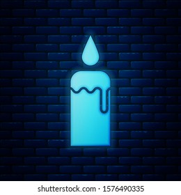 Glowing neon Burning candle in candlestick icon isolated on brick wall background. Cylindrical candle stick with burning flame.  Vector Illustration