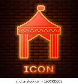 Glowing neon Camping tent icon isolated on brick wall background. Carnival camping tent. Amusement park.  Vector Illustration