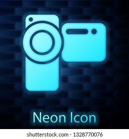 Glowing neon Cinema camera icon isolated on brick wall background. Video camera. Movie sign. Film projector. Vector Illustration