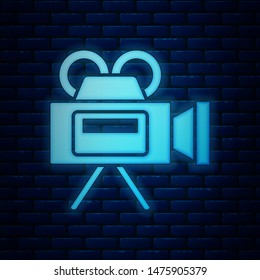 Glowing neon Cinema camera icon isolated on brick wall background. Video camera. Movie sign. Film projector.  Vector Illustration