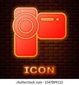 Glowing neon Cinema camera icon isolated on brick wall background. Video camera. Movie sign. Film projector.  Vector Illustration