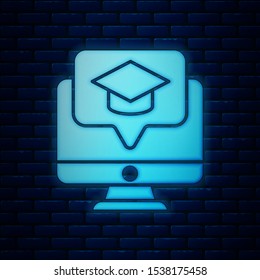Glowing neon Computer monitor with graduation cap icon isolated on brick wall background. Online learning or e-learning concept.  Vector Illustration