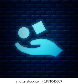 Glowing neon Cube levitating above hand icon isolated on brick wall background. Levitation symbol.  Vector Illustration