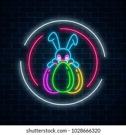 Glowing neon easter bunny with eggs sign in circle frames on dark brick wall background. Night greeting banner with easter rabbit. Vector illustration.