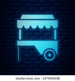 Glowing neon Fast street food cart with awning icon isolated on brick wall background. Urban kiosk.  Vector Illustration