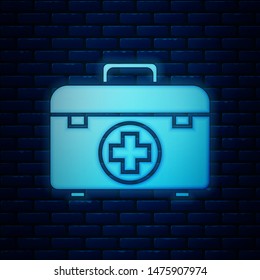 Glowing neon First aid kit icon isolated on brick wall background. Medical box with cross. Medical equipment for emergency. Healthcare concept.  Vector Illustration