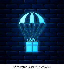 Glowing neon Gift box flying on parachute icon isolated on brick wall background. Delivery service, air shipping concept, bonus concept.  Vector Illustration