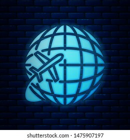 Glowing neon Globe with flying plane icon isolated on brick wall background. Airplane fly around the planet earth. Aircraft world icon.  Vector Illustration