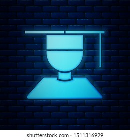 Glowing neon Graduate and graduation cap icon isolated on brick wall background.  Vector Illustration