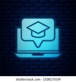 Glowing neon Graduation cap on screen laptop icon isolated on brick wall background. Online learning or e-learning concept.  Vector Illustration
