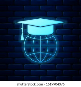 Glowing neon Graduation cap on globe icon isolated on brick wall background. World education symbol. Online learning or e-learning concept.  Vector Illustration